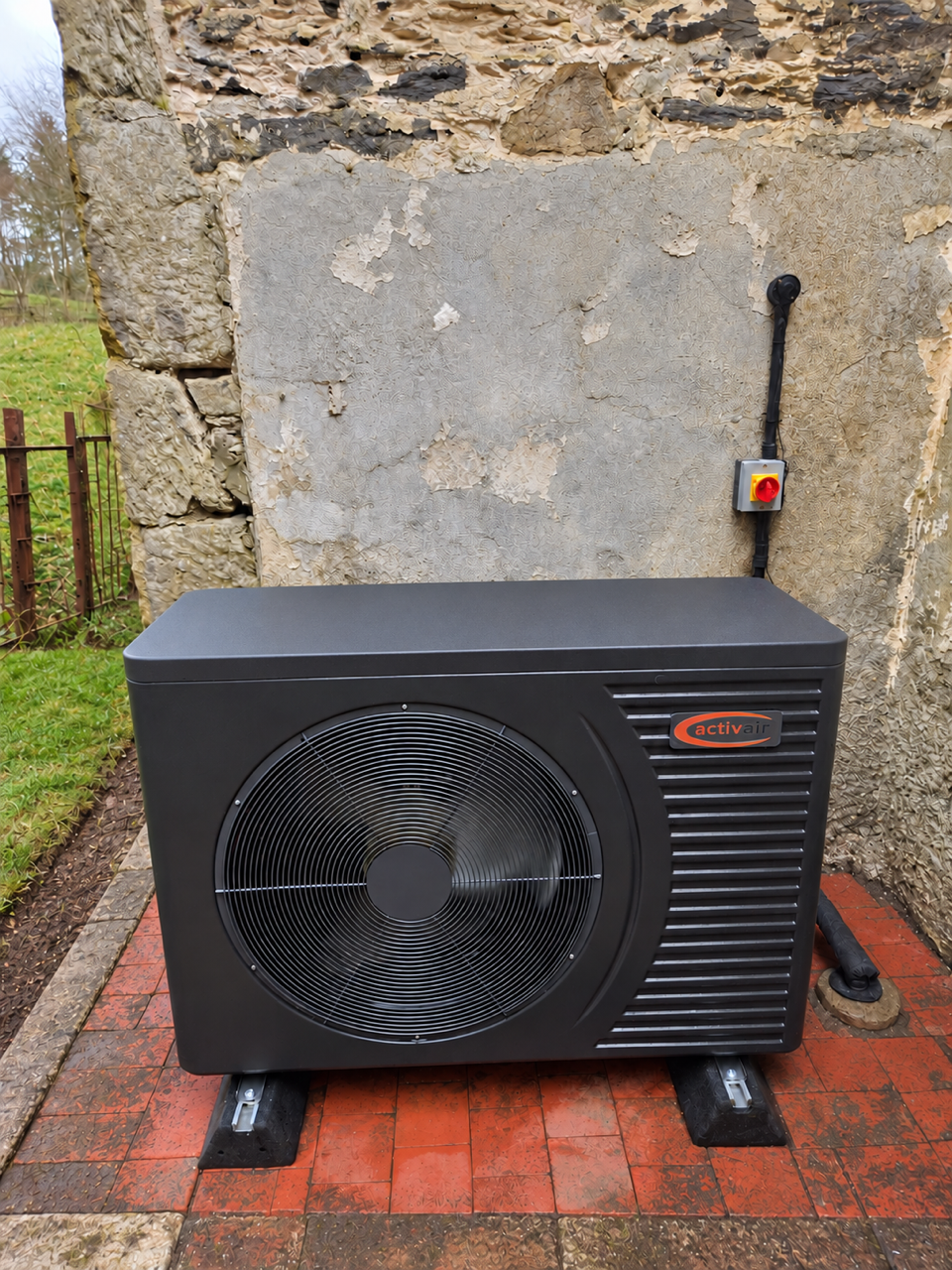 Activair air source heat pump on anti-vibration feet against a traditional stone wall with an isolator switch