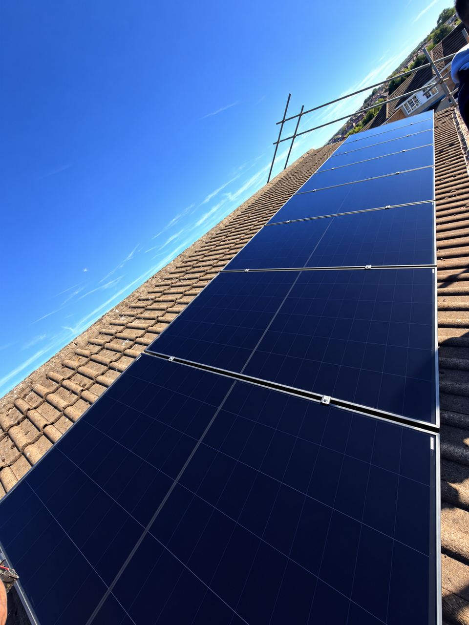 Row of solar panels on a pitched tiled roof with safety scaffolding in place